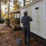 Intervenant nettoyant à la brosse douce le bardage d’un mobil-home sous les pins en automne